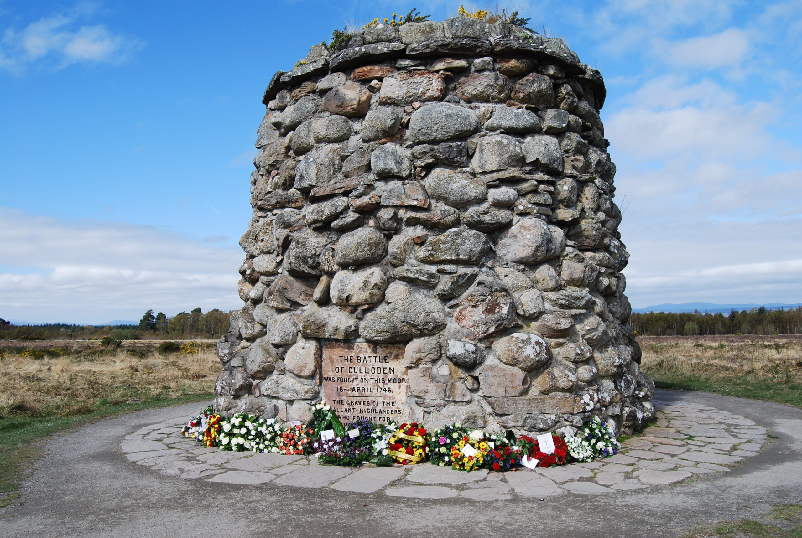 Memorial cairn on site of the Battle of Culloden with floral tributes at the foot.